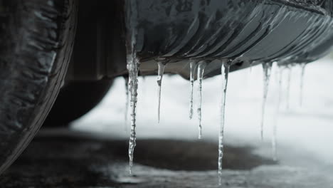 close-up of icy stalactites hanging from a car's mudguard, showcasing frozen textures and the effect of subzero temperatures on vehicle exteriors