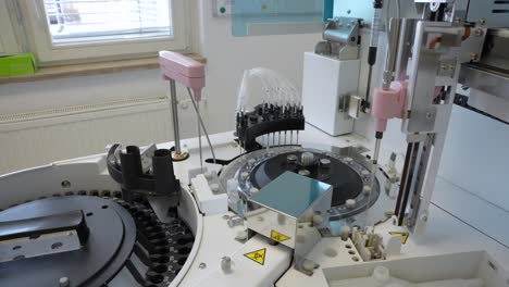 small medical analyzer working on blood samples that are rotating on a disk in laboratory with a box of medical latex gloves in the background near the window