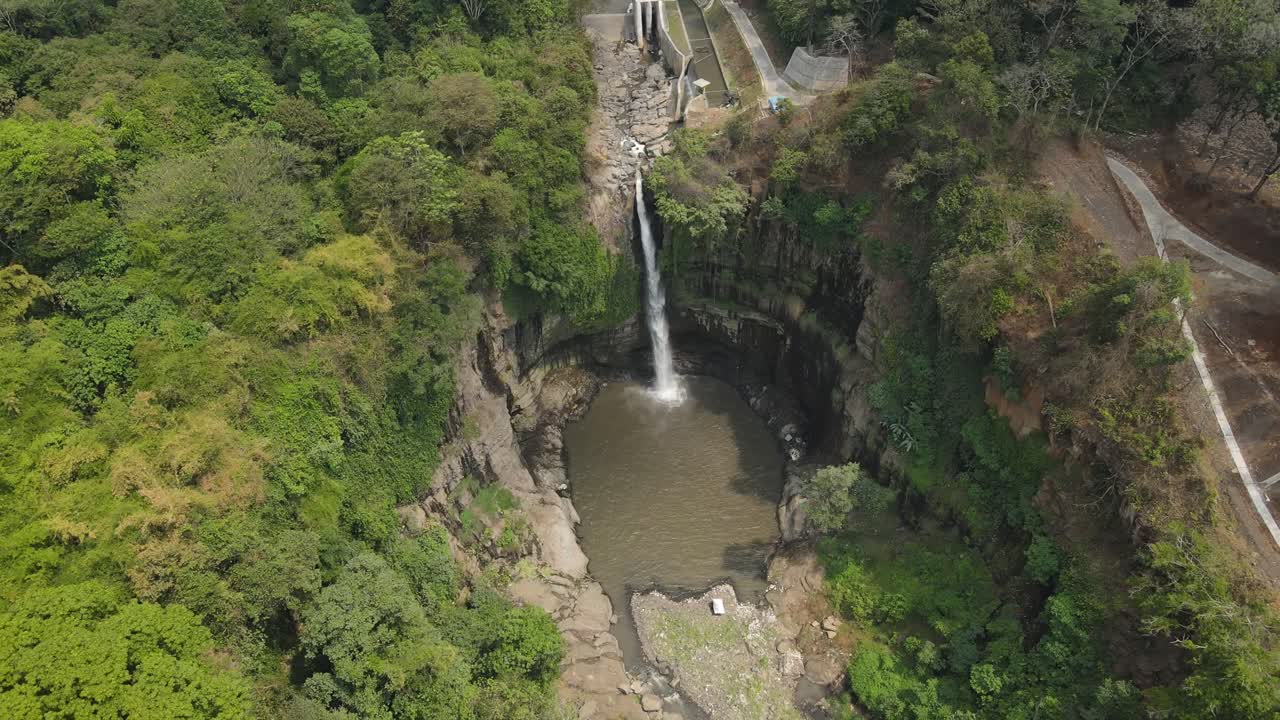 Aerial drone view of tall waterfall flowing into natural pool surrounded by lush tropical forest in Indonesia