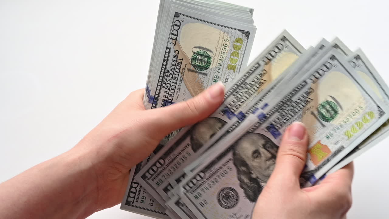 A woman's hands quickly count a stack of one hundred dollar bills against a light background