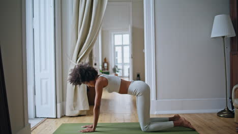 flexible girl cat cow pose practicing indoors. black skin woman bending body mat