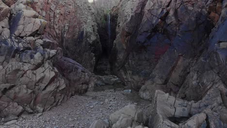 aerial shot, flying into a sea cave at low tide towards a waterfall, plemont bay, jersey, channel islands