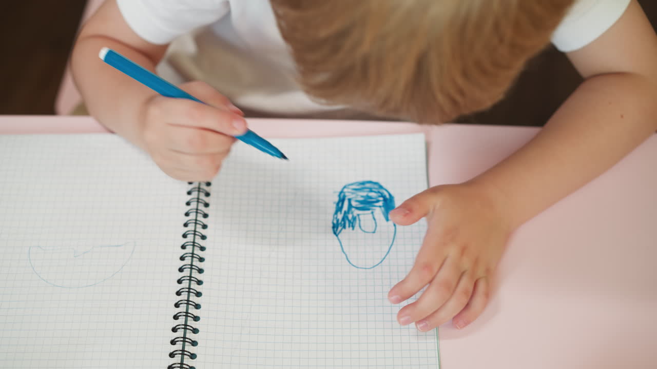Little boy colors doughnut with blue marker in exercise book