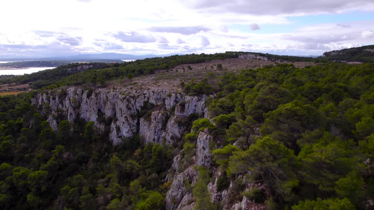 Aerial over natural environment, rock cliffs covered with forest vegetation, daytime capture, revealing water surface in distance