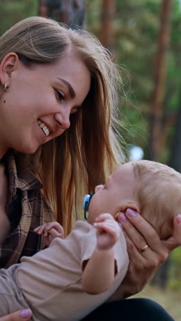 mom communicating with her baby in nature. long-haired woman holding her beloved infant and kissing him. vertical video