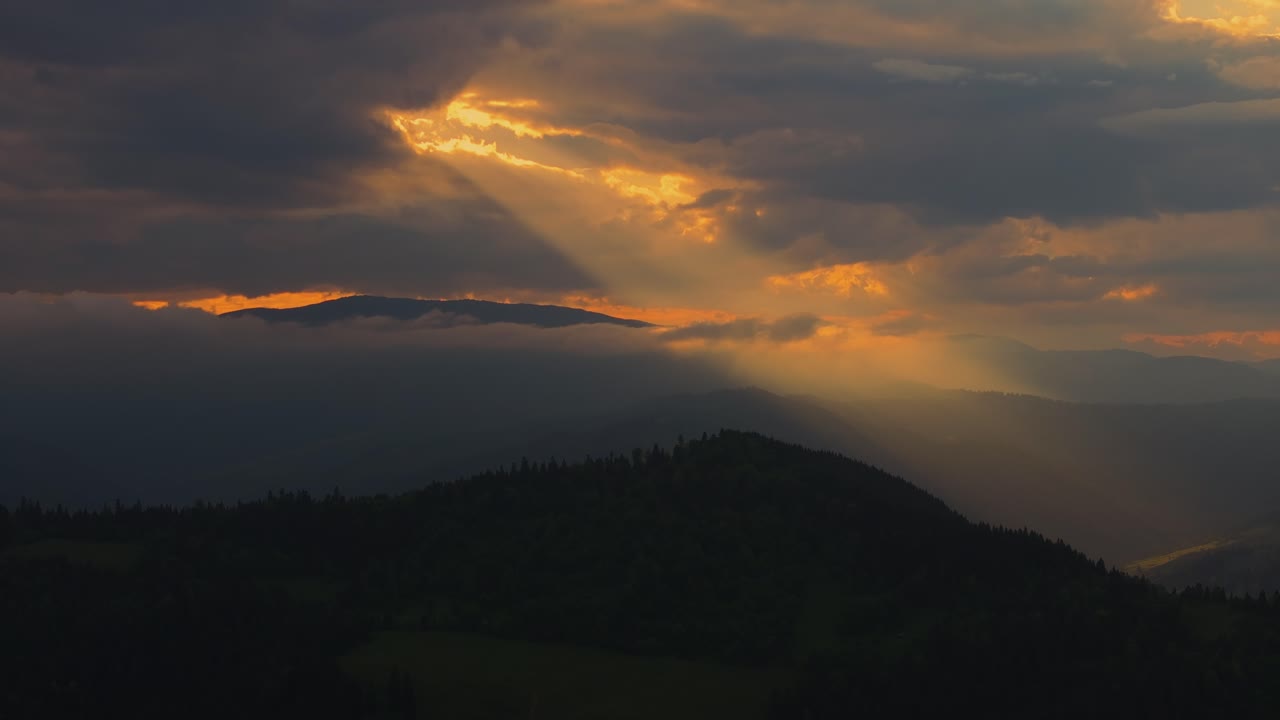 fotografía aérea que muestra rayos de sol naranja atravesando las nubes, iluminando cadenas montañosas lejanas, alto contraste