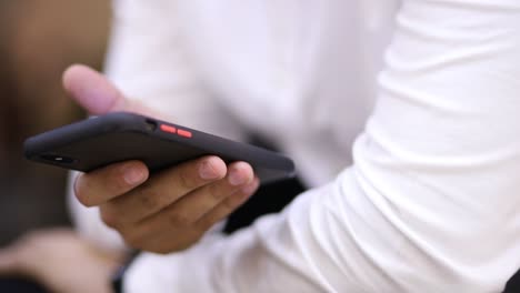 Close-up-shot-of-an-Hispanic-young-man-holding-a-smartphone-and-surfing-through-it