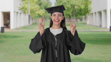 feliz chica graduada de la universidad india mostrando el signo de victoria