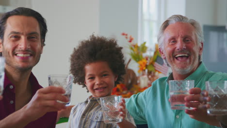 Multi-Generation-Family-Celebrating-Thanksgiving-At-Home-Eating-Meal-And-Doing-Cheers-With-Water