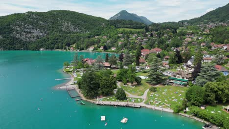 people swim and relax at turquoise blue lake annecy in french alps - aerial