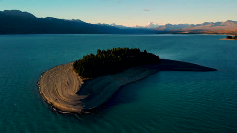 Aerial-pull-back-of-small-forested-island-in-famous-Lake-Pukaki,-golden-hour