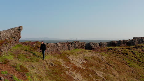 Drohnenblick-Vogelperspektive-Junger-Mann-Backpacker-Explorer-Wanderweg-über-Felsformation-In-Island.-Luftaufnahme-Ein-Wanderer,-Der-Auf-Einen-Steinhügel-Klettert-Und-Die-Schönheit-Der-Natur-Genießt