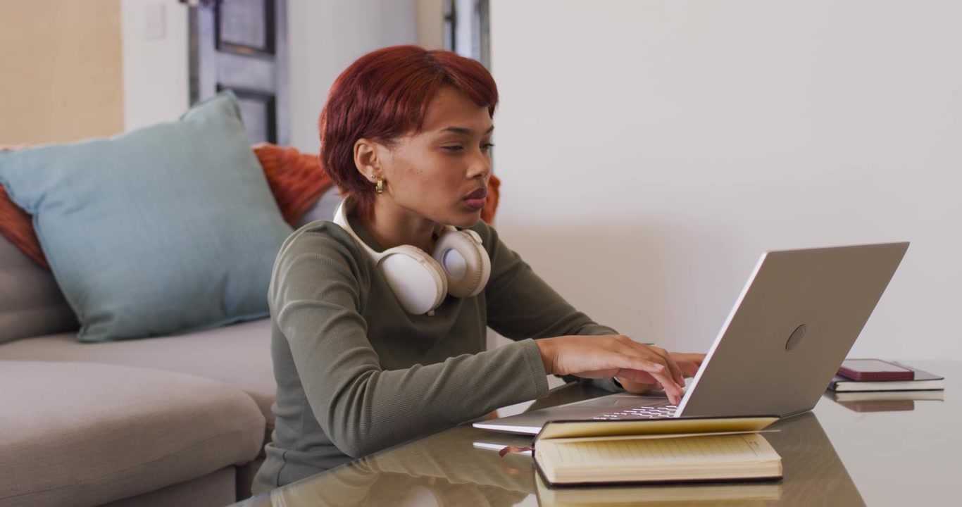 African American woman feeling eye strain rubbing face raising headphones typing on laptop at home