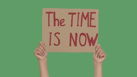 female hands hold a poster from a cardboard box with the words the time is now. protest against racism and police brutality. isolated a green screen, chroma key. close up. slow motion