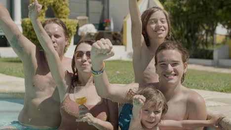 feliz familia caucásica parada en la piscina y levantando los brazos mientras mira la cámara