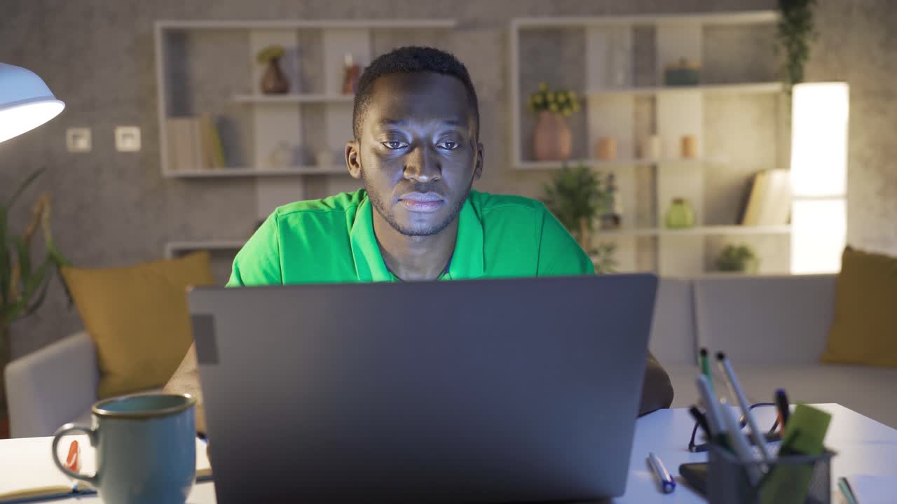 Afroamerikanischer Mann schaut auf den Computerbildschirm und arbeitet sehr sorgfältig.