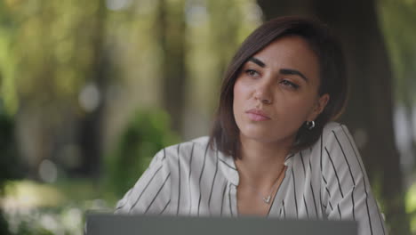 mujer seria y talentosa morena de grupo étnico hispano se sienta en una mesa en un café de verano con una computadora portátil. considera resolver problemas. mujer de negocios desconcertada. retrato de una hermosa mujer de negocios