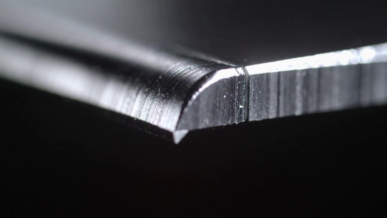 Riflesso cangiante che crea un bordo smussato, rivelando le linee di molatura su sfondo nero ed esponendo una scheggiatura