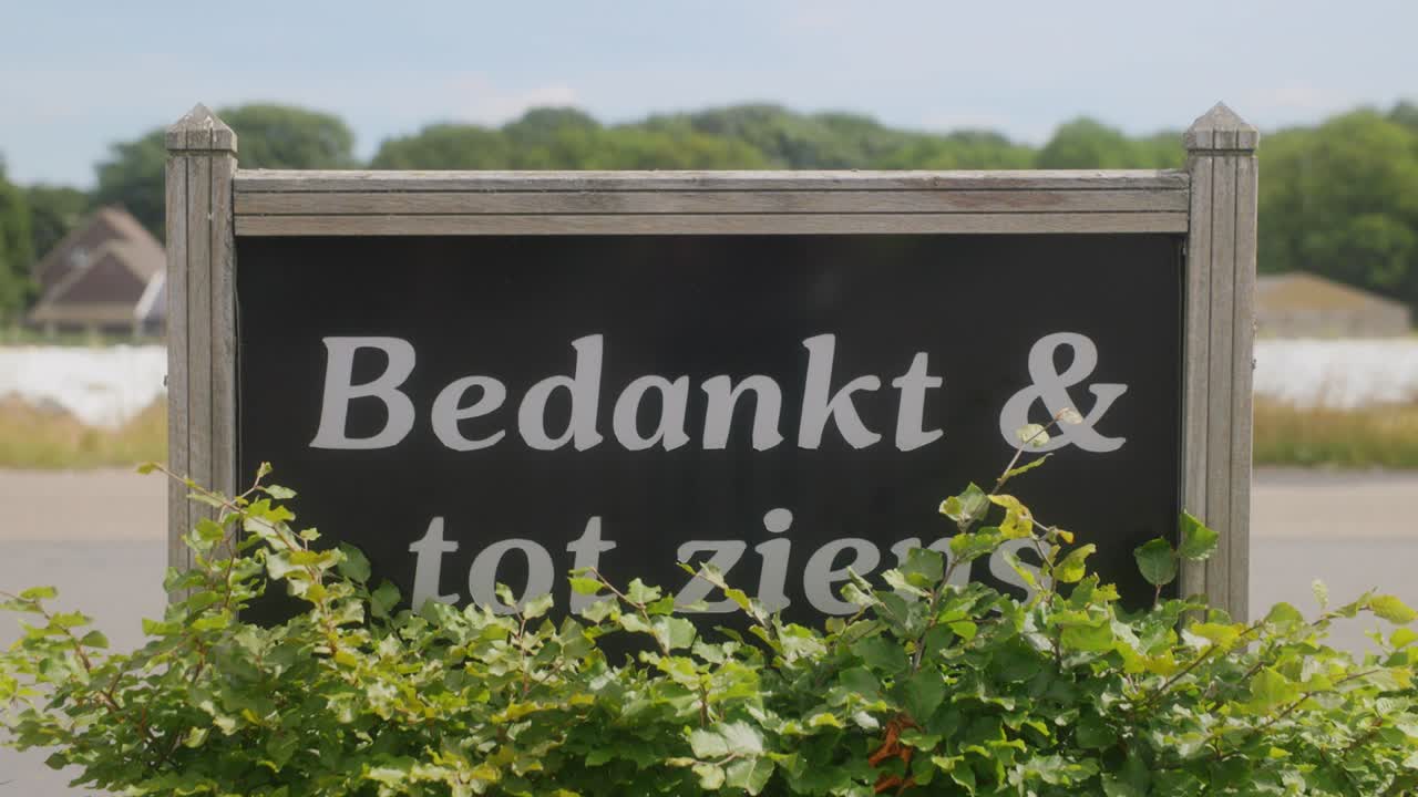 A welcome and goodbye sign in Dutch of a company with green bushes around it