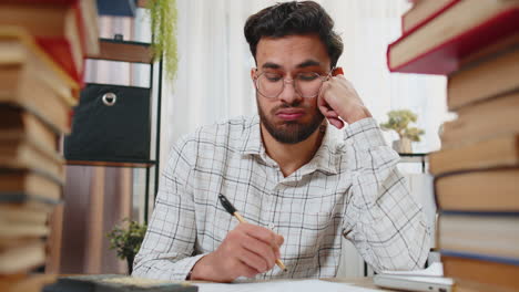 Stressed-tired-freelancer-businessman-touching-head-in-despair-surrounded-by-stack-of-books-on-table