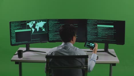back view of asian man developer working with mobile phone while write code with multiple computer screens in green screen studio