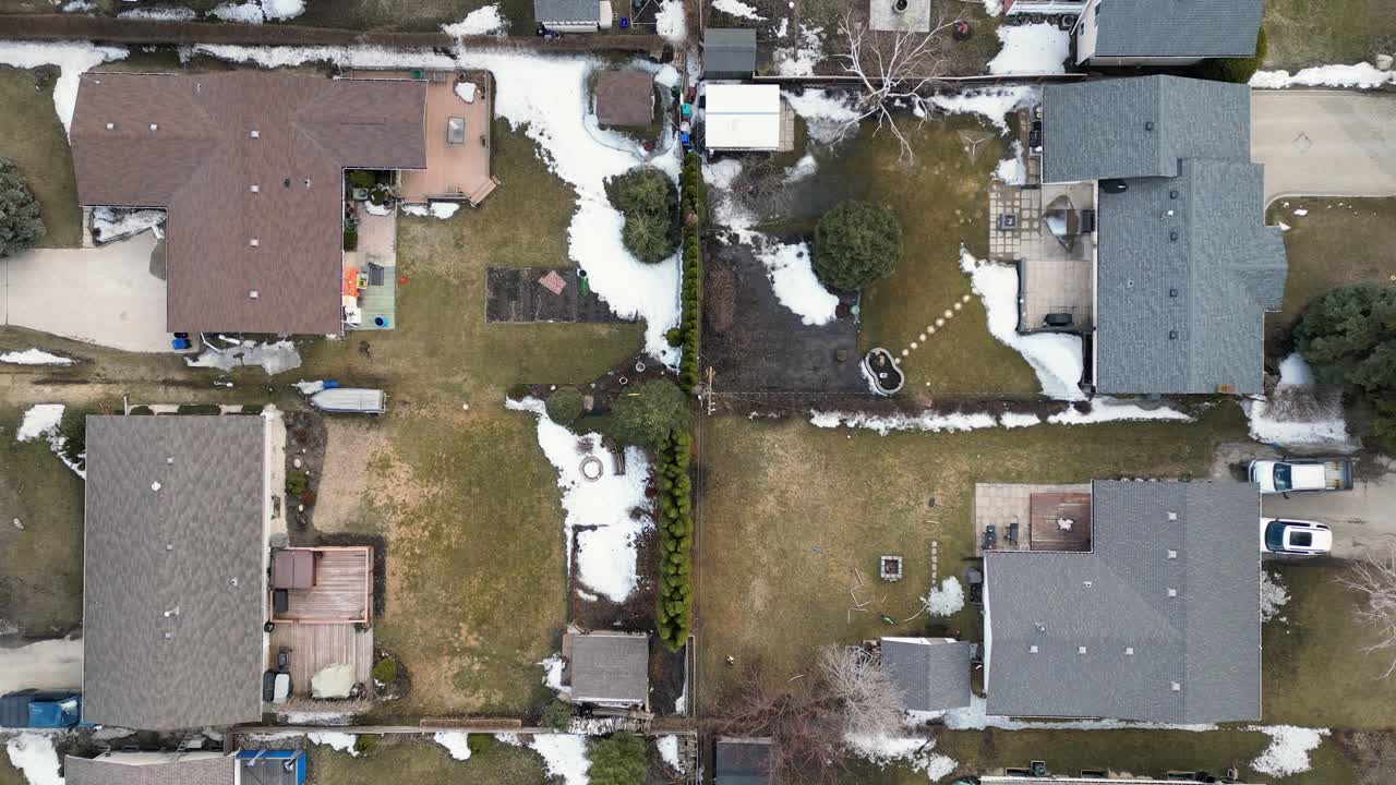 Top down drone shot of four snowy backyards as the camera rises to reveal surrounding homes