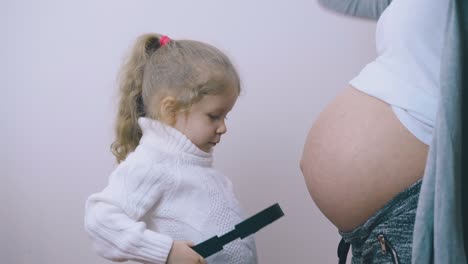 niña pequeña pone auriculares en la cintura con la ayuda de la madre embarazada