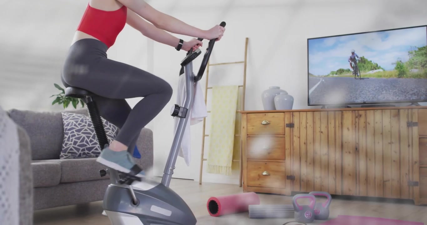 Sovrapposizione di codice traslucido pulsante, donna che pedala su una cyclette a casa seguendo filmati di ciclisti in TV