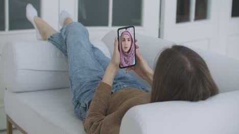 Frau-Nutzt-Medizinische-App-Auf-Dem-Smartphone-Und-Berät-Sich-Per-Videokonferenz-Mit-Einer-Arabischen-Muslimischen-Frau-Im-Hijab-Arzt.-Frau-Nutzt-Online-Chat,-Um-Mit-Familientherapeuten-Und-Einer-Coronavirus-Pandemie-Zu-Sprechen.