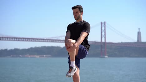 athletic man stretching leg at riverside