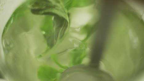 close up of a spoon stirring mint leaves inside a glass