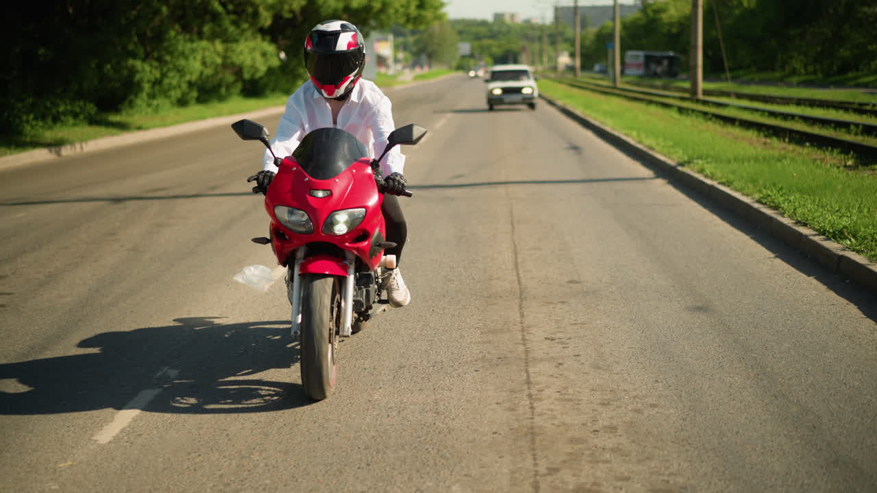 un motociclista con casco disminuye la velocidad en respuesta al tráfico, con una pieza de cuero blanco moviéndose cerca y una vista borrosa de un coche con faros acercándose por detrás