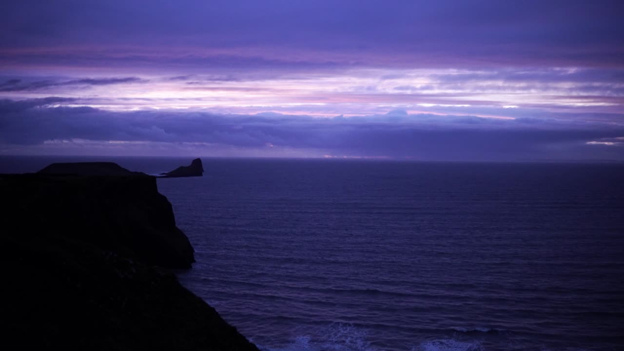 puesta de sol púrpura sobre los acantilados y una pequeña isla, ventosa