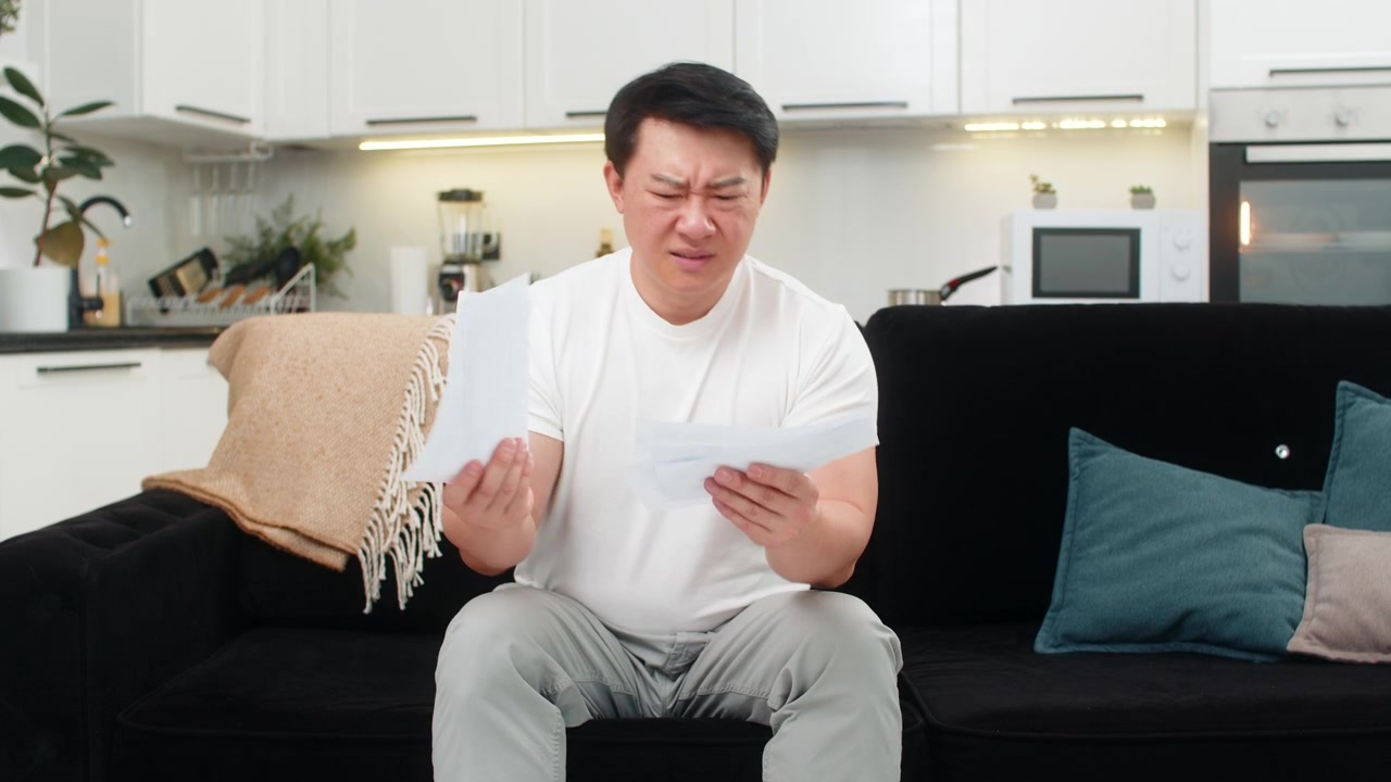 アジア系の男性が、怒って紙幣を投げ捨てた後、心を落ち着かせ、書類を拾い上げ、冷静かつ明確な決意をもって計画を実行する。