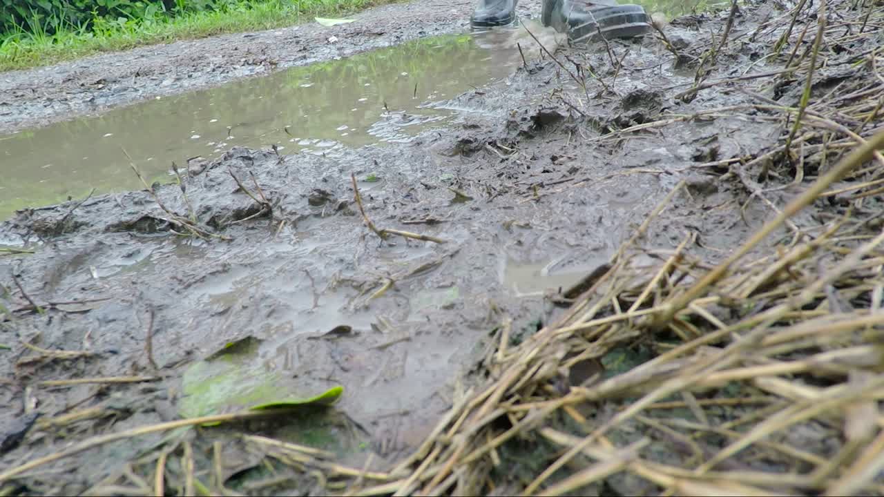 카메라를 통과하는 진흙 투성이의 땅을 걷는 부츠의 샷