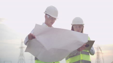 a group of engineers at a high-voltage power plant with a tablet and drawings walk and discuss a plan for the supply of electricity to the city. transportation of renewable clean energy.