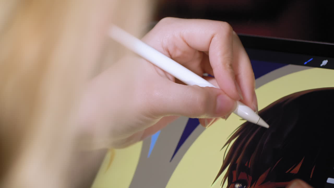 An artist paints with a digital pen on a tablet, making a digital painting, over the shoulder of a blonde woman