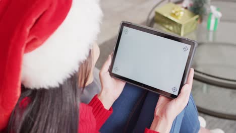 Biracial-woman-with-santa-hat-using-tablet-with-copy-space