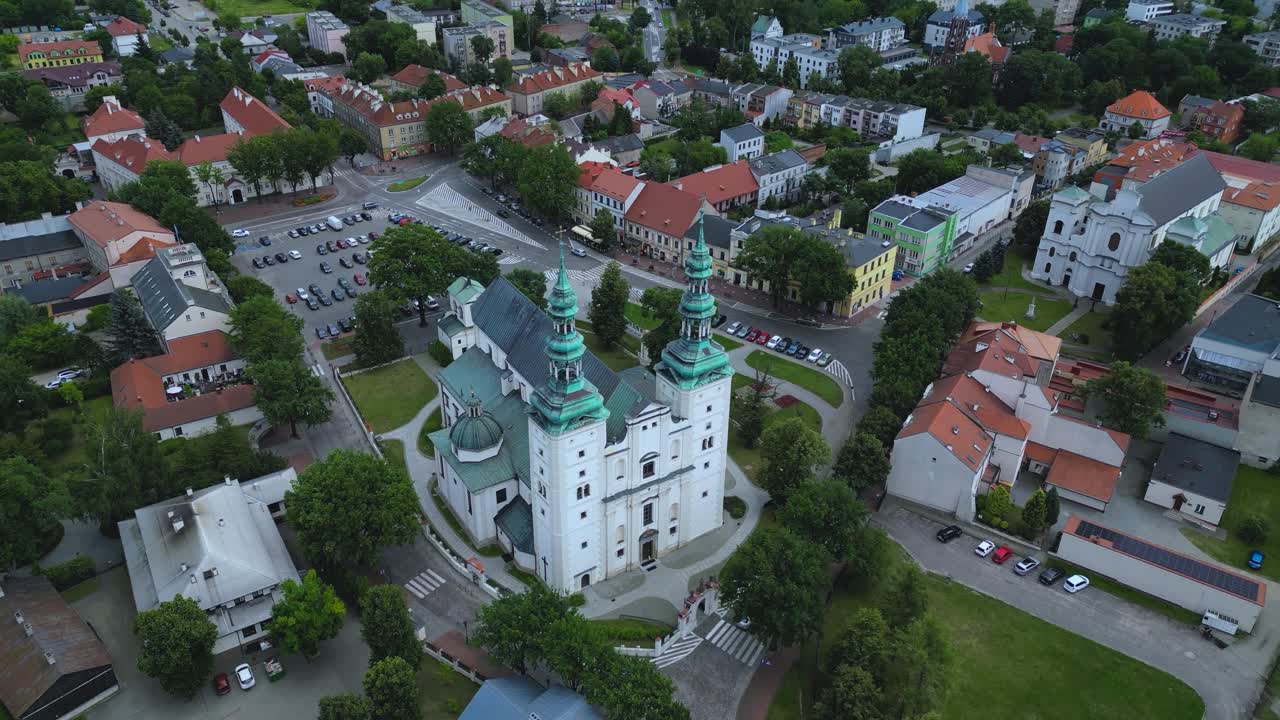 The stunning architecture of the historic Łowicz Cathedral Basilica and its twin green towers. Sweeps over the surrounding cityscape of Łowicz, Poland, showcasing the urban landscape