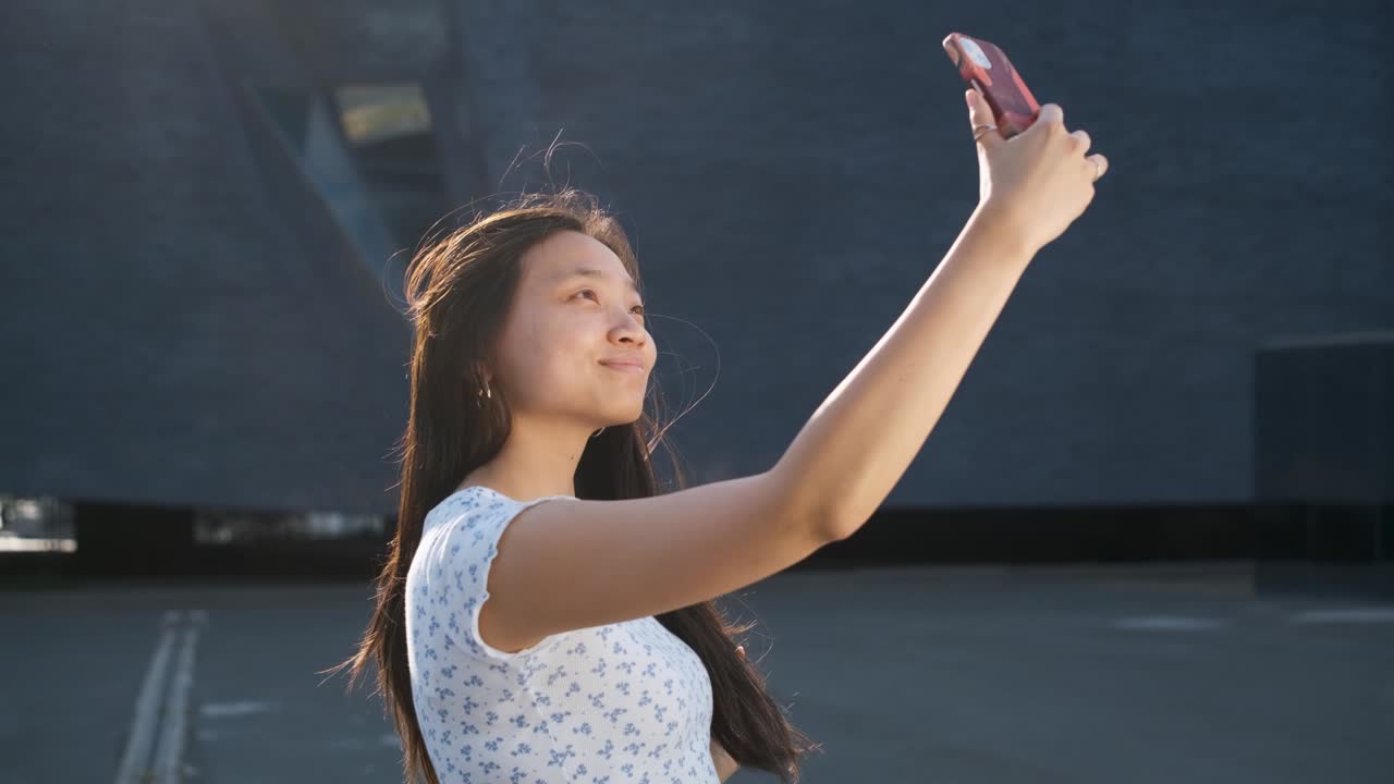 Young confident woman posing while taking selfies with a mobile phone outdoors.