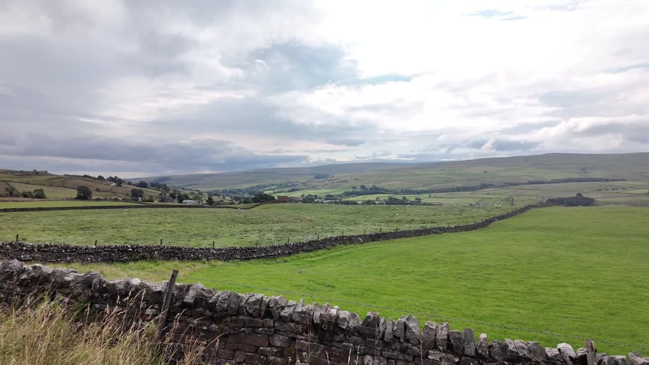 Scenic landscape in North Pennines National Landscape, England, showcasing dry stone walls, green fields, and rolling hills under a cloudy sky