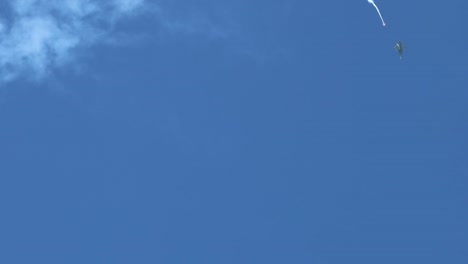 parachutes gracefully descend through a vast, clear blue sky with scattered clouds.