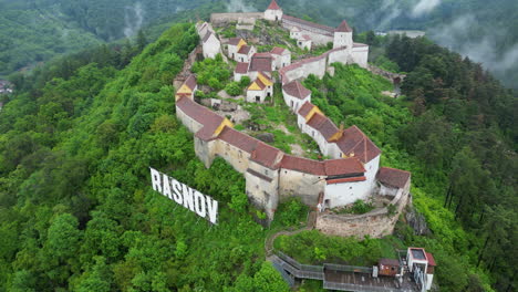 aerial view rasnov citadel, a medieval fortress perched on a hilltop in romania, surrounded by lush green forest