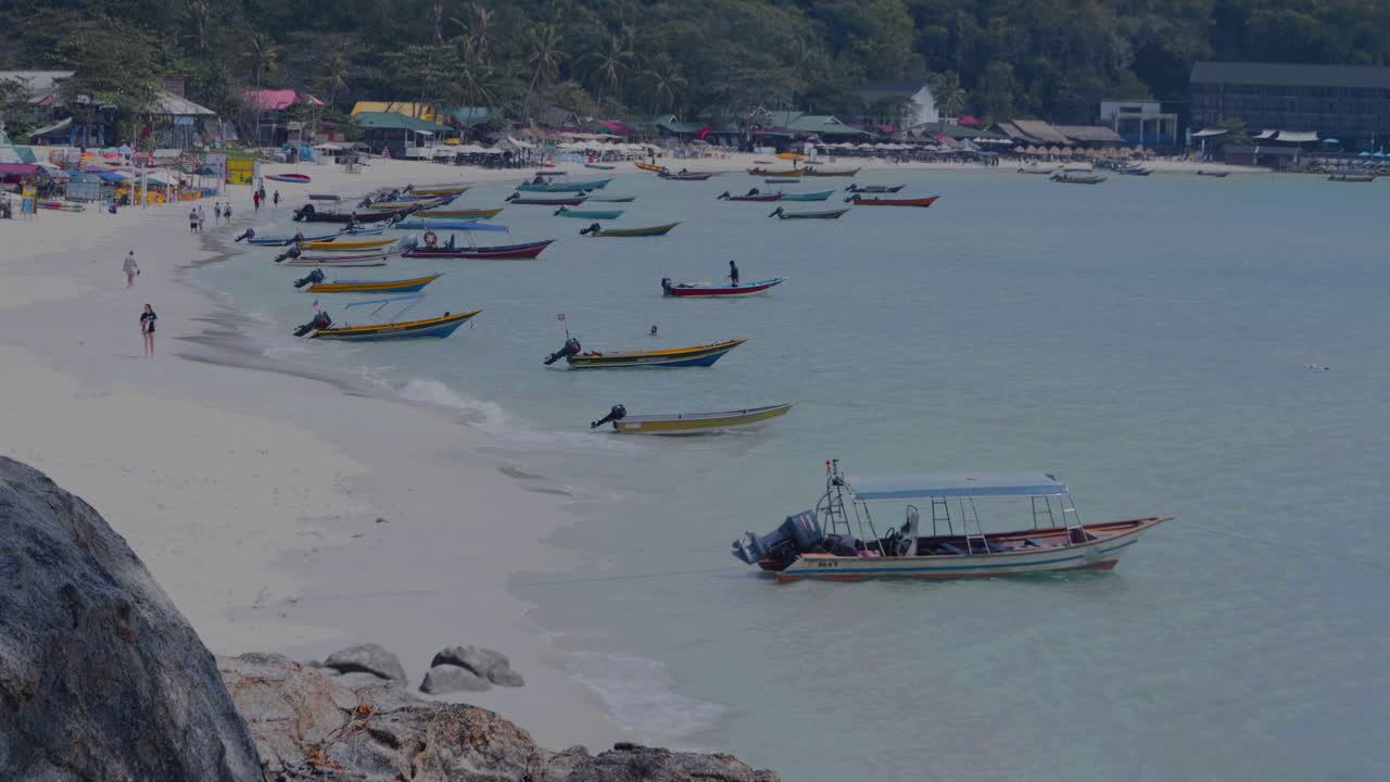 Longtail boats gently sway on the crystal-clear turquoise water, resting near the sandy shore of tropical beach, creating a serene and picturesque scene of tranquility and escape in Langkawi Malaysia
