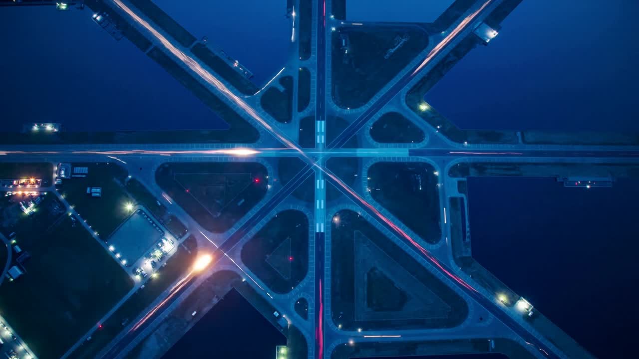 Mostra uno svincolo a stella che crea scie di traffico notturne, con fari opposti che si incontrano causando un bagliore.