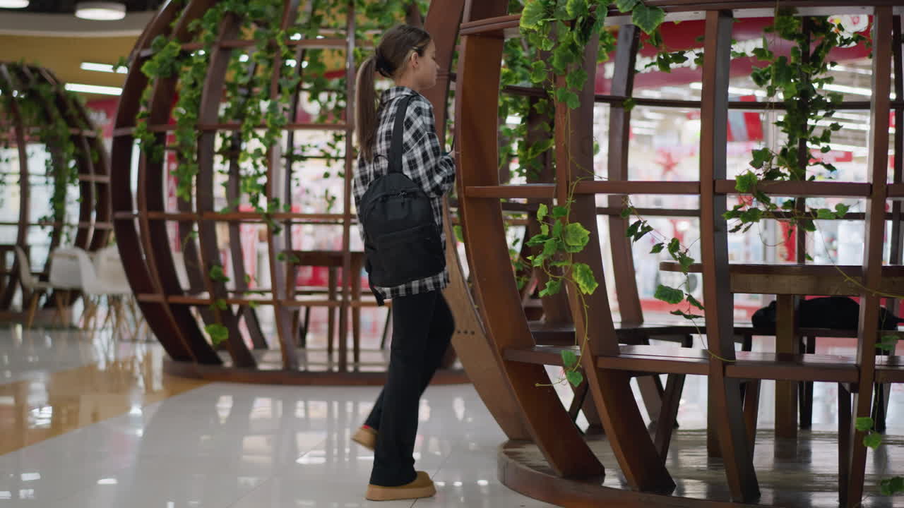 젊은 소녀는 초록색으로 장식된 우아한 목조 좌석 구조를 특징으로 한 현대적인 실내 공간에서 그녀의 좌석을 향해 차분하게 걸어 가며 세련되고 편안하고 조용한 분위기를 만니다.