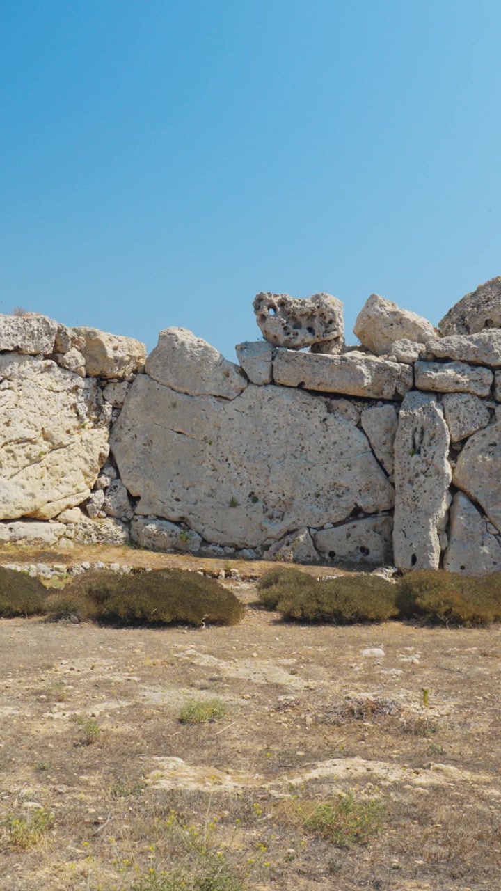 Video verticale di antiche rovine megalitiche in pietra con blocchi di calcare erosi sotto un cielo azzurro brillante, perfetto per storie e reel.