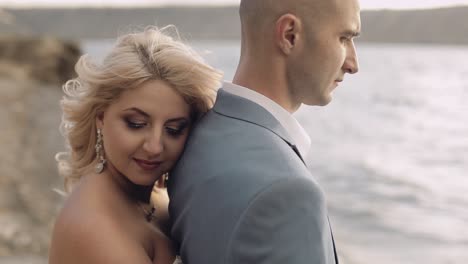 newlyweds stand on the riverbank. the bride hugs the groom. wedding couple