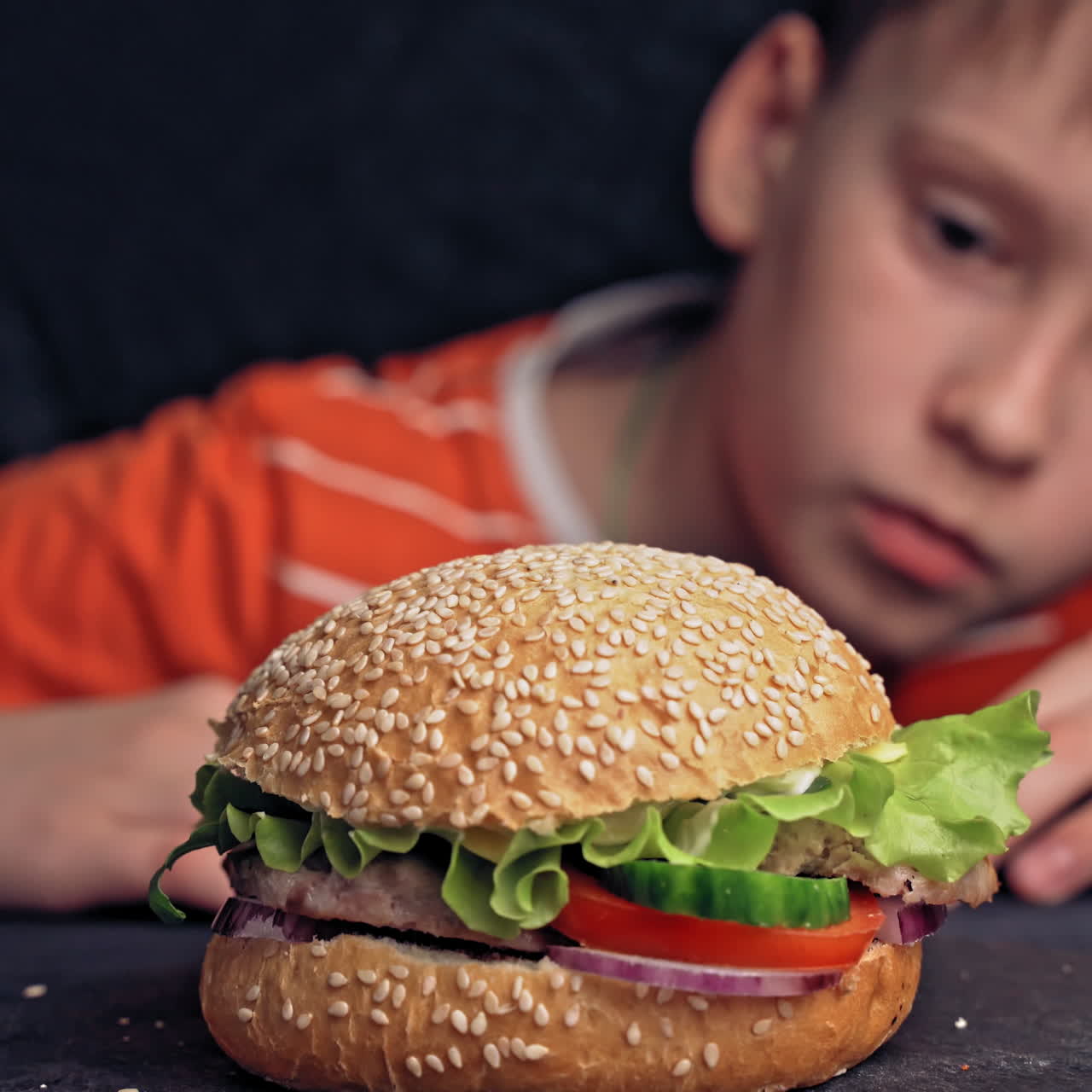 Un ragazzo che assaggia un gustoso grande hamburger, fast food.