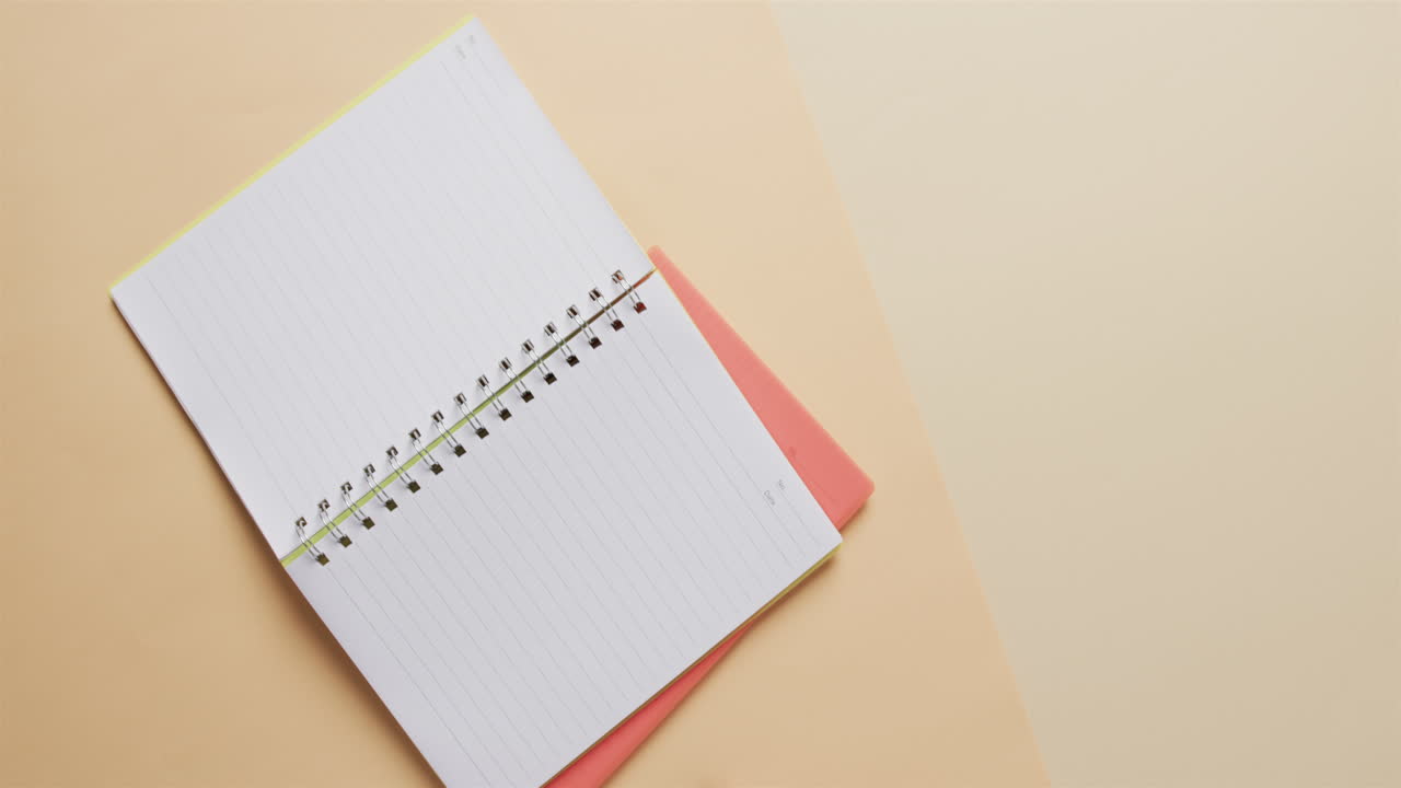 Overhead view of open notebook with pink marker with copy space on beige background, in slow motion